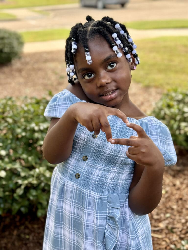 Child making a heart shape with her hands and smiling.