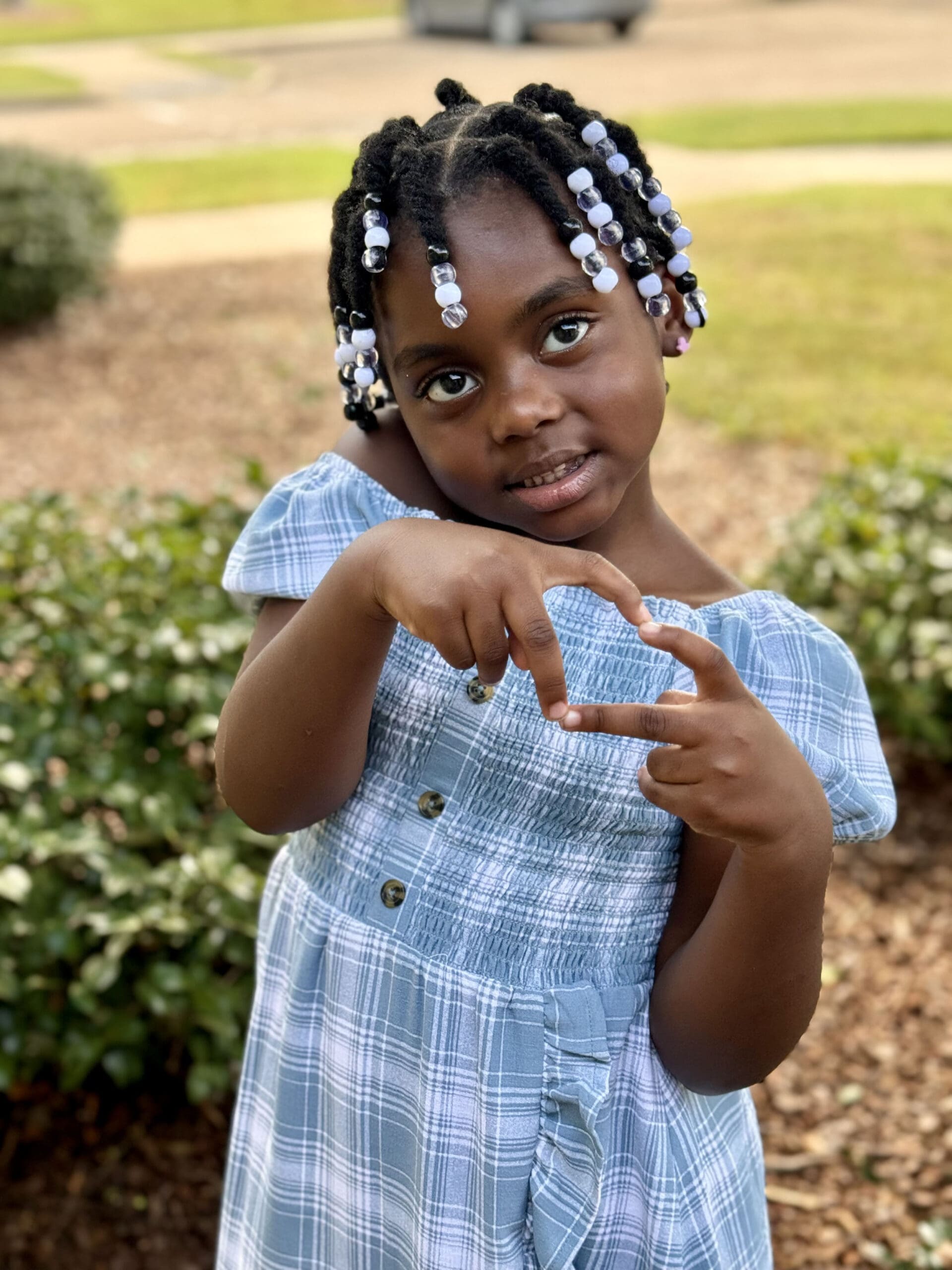 A young child outside making a heart shape with her hands.