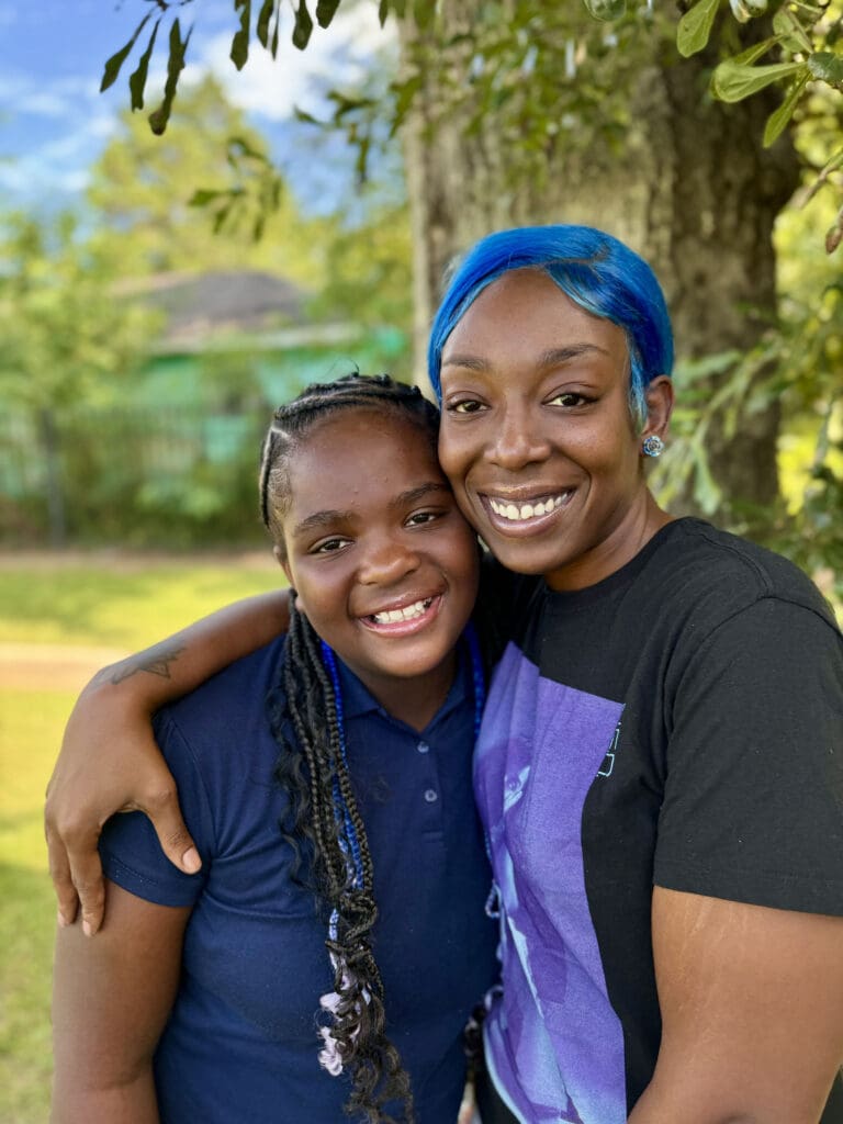 Mother with her arm around her child outside smiling.