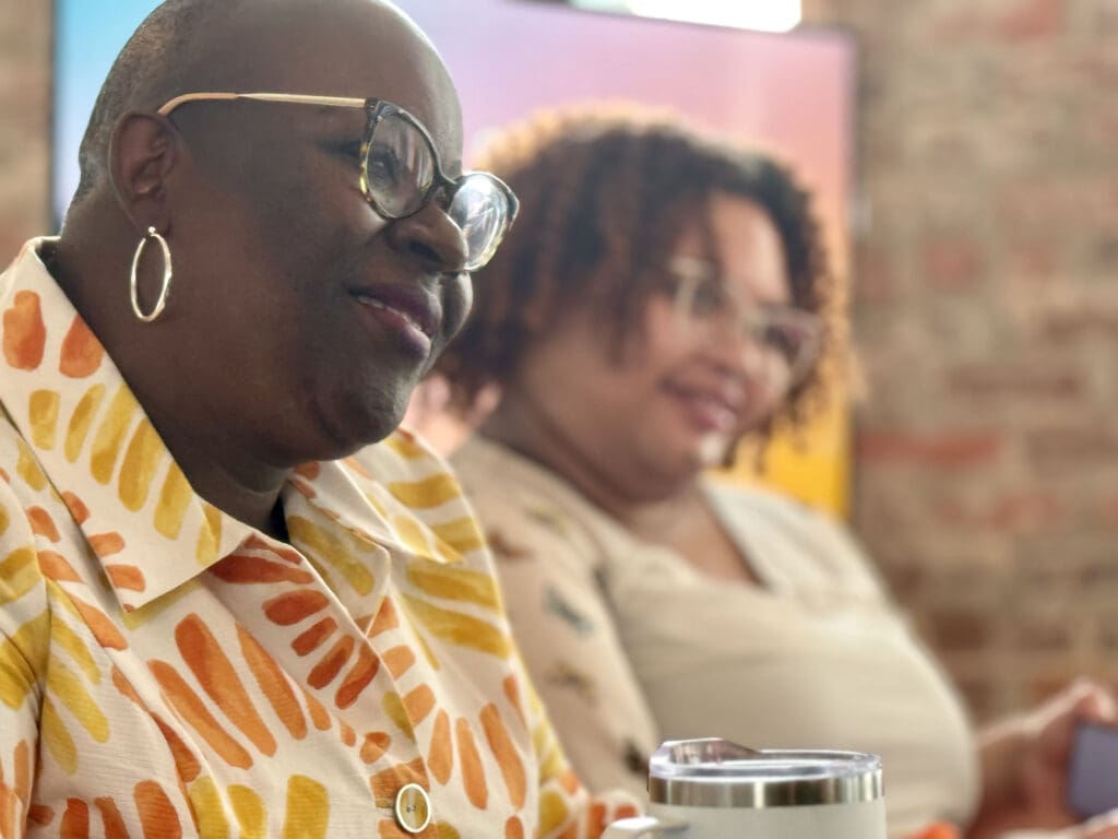 Mother with glasses smiling and listening to someone speak.